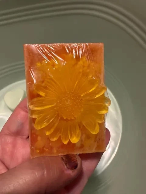 A square bar of amber handmade soap with a flower pattern, held in a hand.