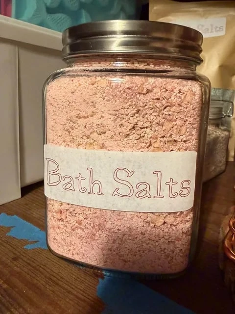 Pink bath salts in a glass jar with a handwritten Bath Salts label.