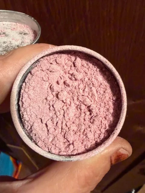 An open silver tin of pink blush powder.