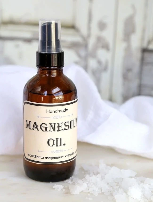 An amber glass spray bottle of magnesium oil with coarse salt flakes in front of it.