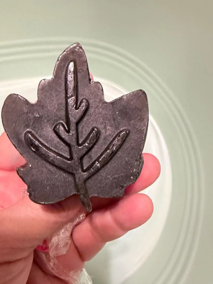 A dark brown leaf-shaped pecan soap held in a hand.