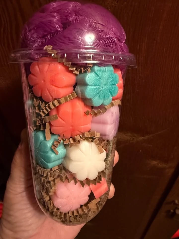 A cup of small orange, teal, pink and cream flower soaps topped with a purple pouf.