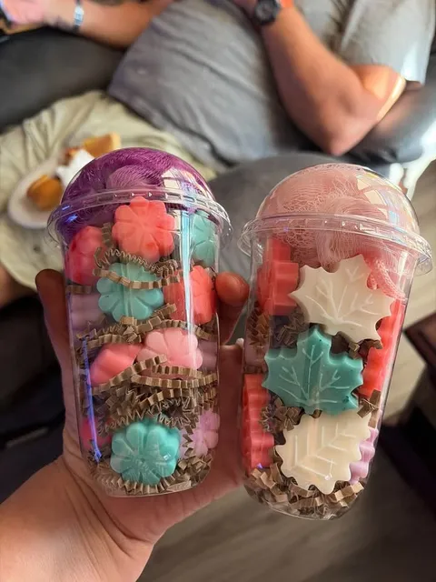 Two cups of small flower and leaf soaps topped with poufs.